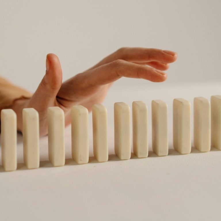 Persönliche Betreuung Eine Hand berührt eine Reihe aufrechter Dominosteine.