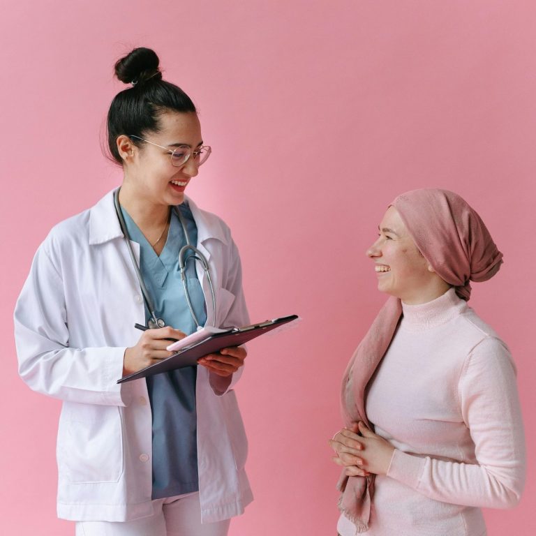Onkologie Ärztin im weißen Kittel spricht freundlich mit Patientin in rosa Kopftuch.